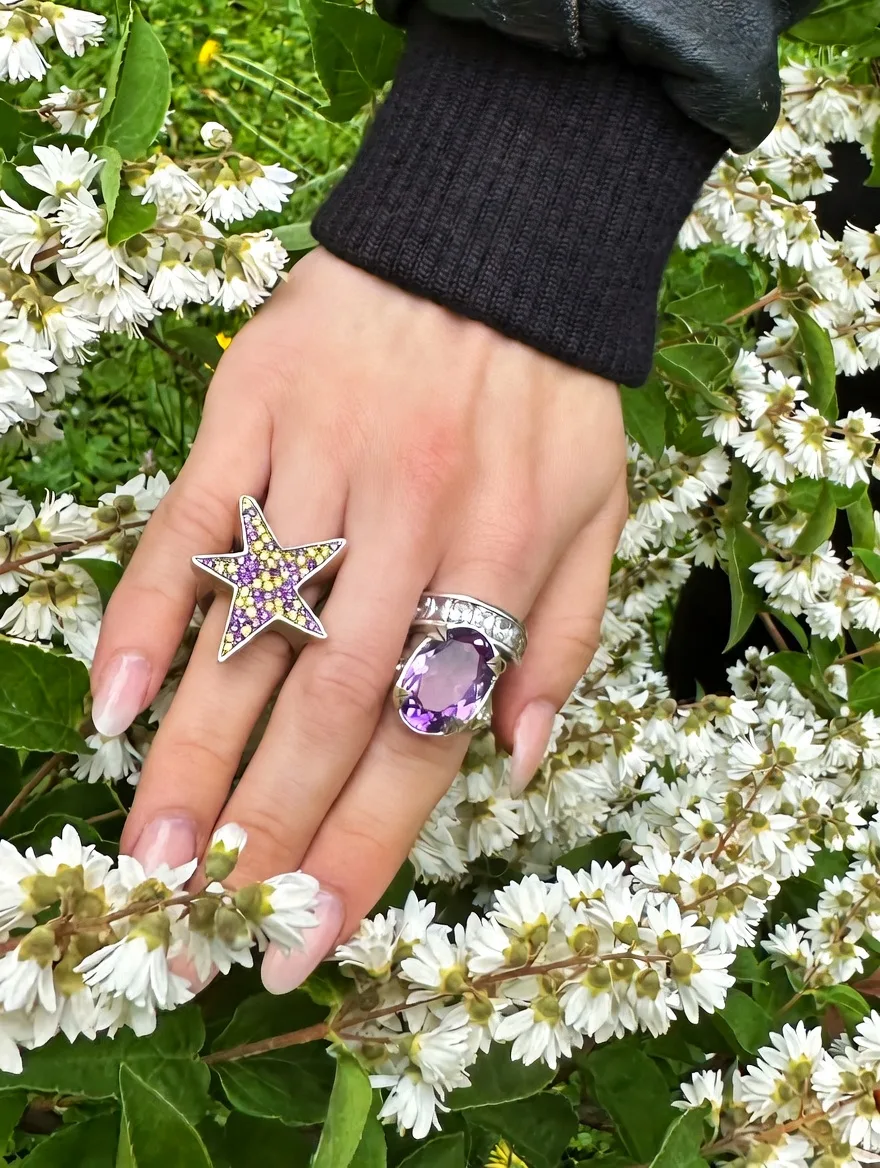 Hand mit drei Silberringen vor weißen Blüten: großer Amethyst-Ring, Channel-Ring und Stern-Siegelring